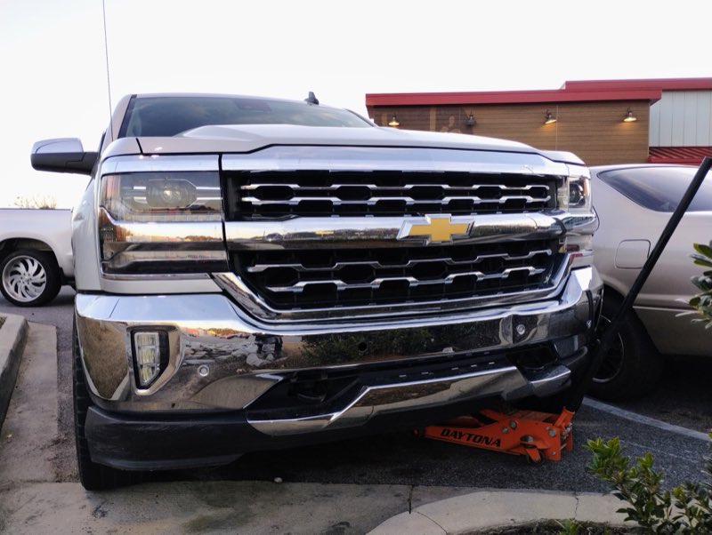 Close-up of a chrome Chevrolet Silverado grille with a floor jack under the bumper