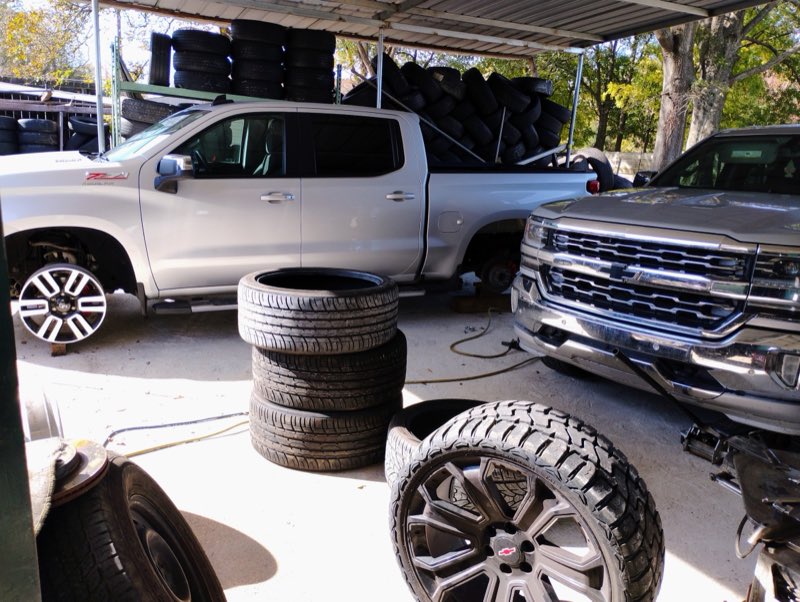 Two trucks under the shop awning with stacks of tires behind them